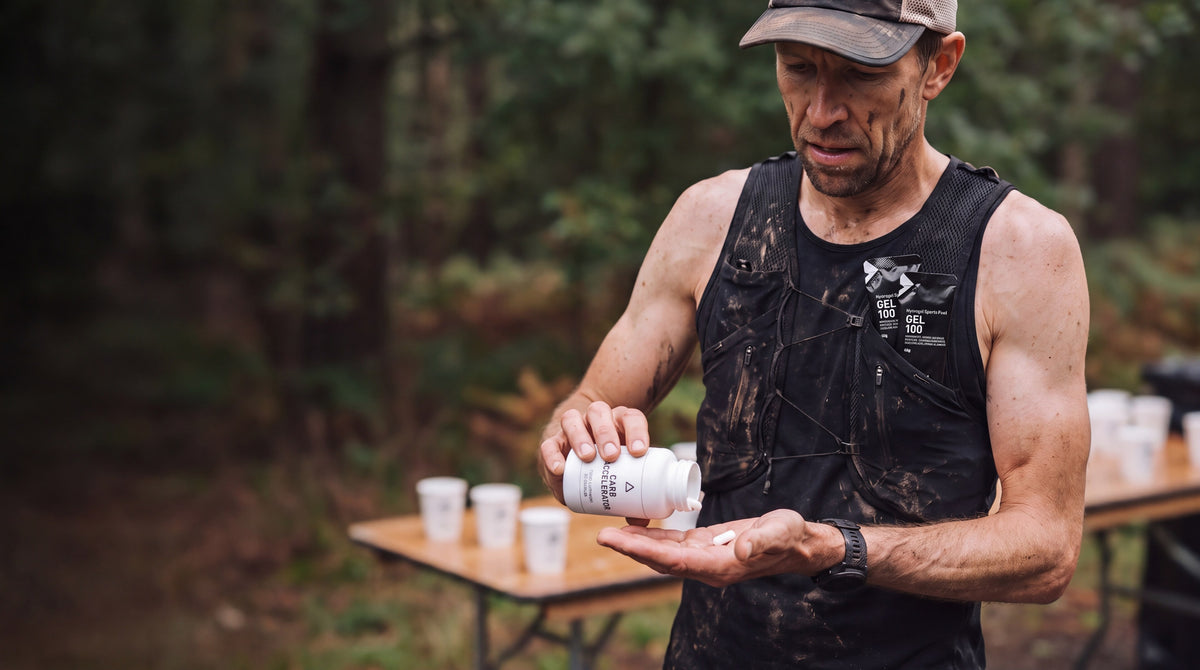 Ultra runner at a trail aid station taking a Carb Accelerator capsule, Maurten gels in his vest